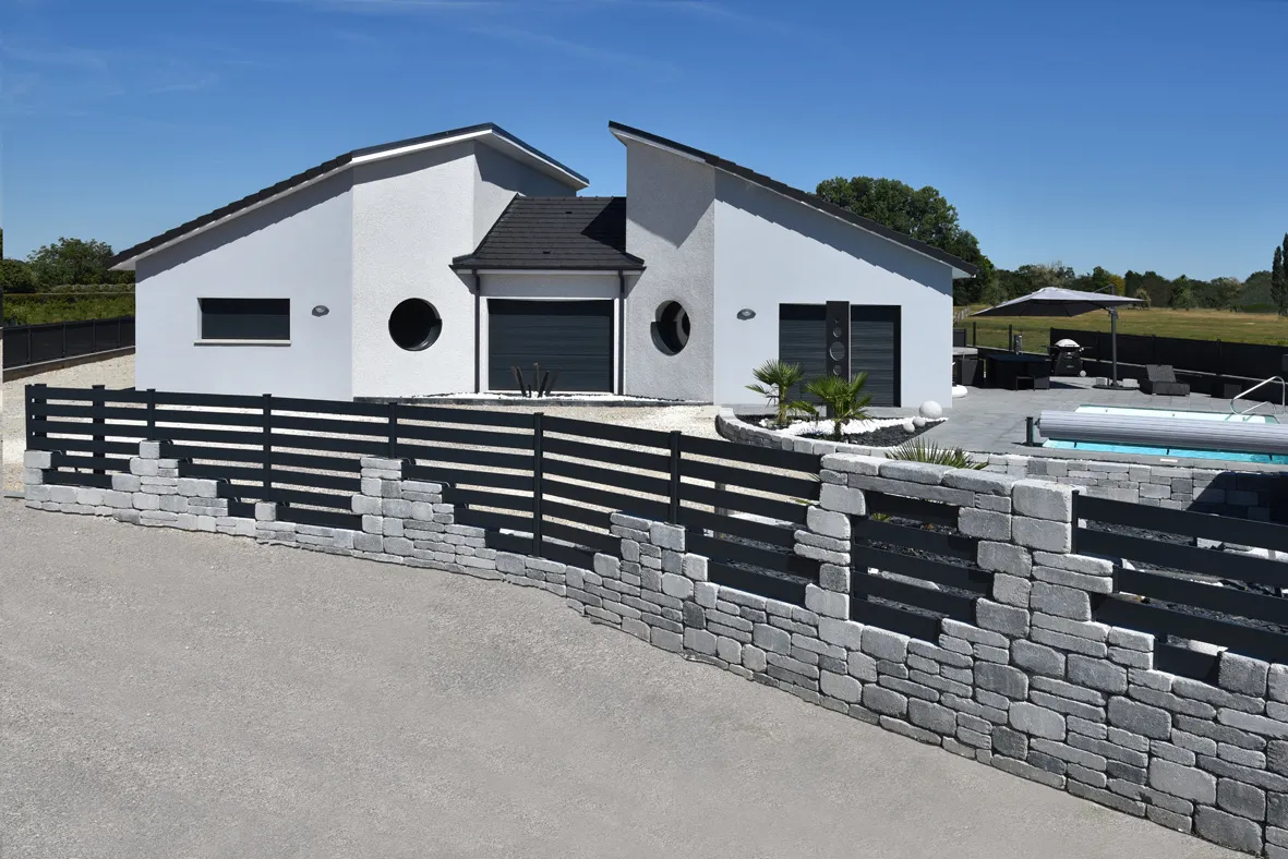 Clôture en aluminium moderne avec éléments en pierre, entourant une maison contemporaine avec piscine<br />
