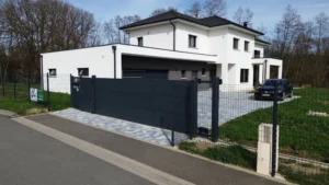 Portail moderne en aluminium noir installé devant une maison contemporaine avec une allée pavée et une clôture métallique