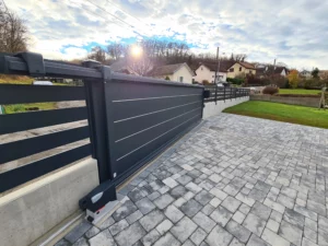 Portail coulissant en aluminium avec lignes décoratives, installé devant une maison avec une allée pavée