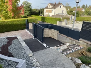 Portail télescopique en aluminium, installé devant une maison avec une allée pavée et un jardin paysager